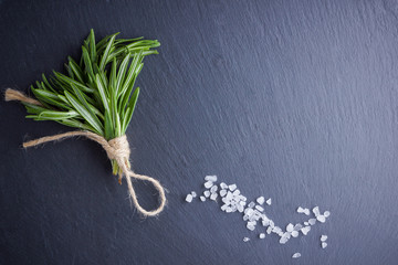 Rosemary bundle tied with twine on a black background. Fresh rosemary and salt on slate stone. Herbs for cooking meat dishes with copy space. Top view