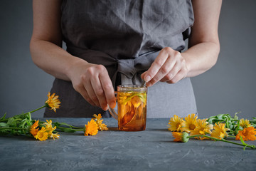 Woman making healthy tea with calendula or marigold flowers. - Powered by Adobe