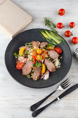 Gourmet salad with smoked duck breast, cherry tomatoes, orange and pine nuts, flavoured with citrus dressing on a white wooden table with fresh ingredients on it