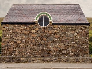 Facade of and old stone building with round window and tiled roof, Brown color of the material, © mark_gusev