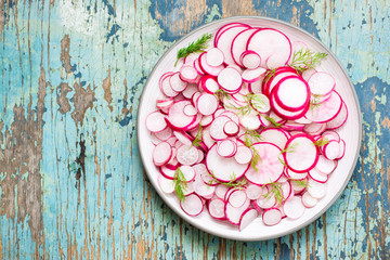 Fototapeta na wymiar Fresh salad of radish and dill on a plate on a wooden table. Top view