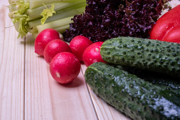 fresh vegetables on a light wooden table, paprika, celery, leaves of lettuce, cucumbers and radishes