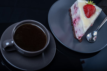 cream fruit cake and a cup of black coffee on a black glass table