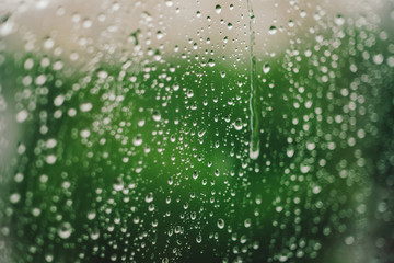 Window glass with drops of rain. Atmospheric green background with raindrops in bokeh. Droplets close up. Detailed transparent texture in macro with copy space. Rainy weather. Insulation concept.
