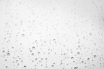 Window glass with drops of rain. Atmospheric light monochrome background with raindrops in bokeh. Droplets close up. Detailed black-white texture in macro with copy space. Rainy weather in grayscale.