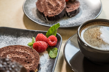 Chocolate swiss roll with jam decorated with raspberries on a plate and black coffee on the table. Selective focus.
