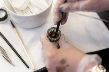 Beauty brows care concept: master is mixing henna for eyebrows coloring. swatches on hand in glove