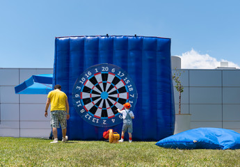 Dad and boy having fun with giant inflatable dart board outside/outdoor.