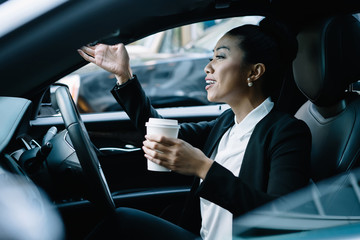 Stressful female entrepreneur with caffeine beverage in hand gesturing and yelling because of late to business meeting in company office of corporate enterprise, concept of automobile congestion