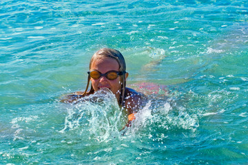 happy girl swims in swimming glasses in the clear sea with splashes