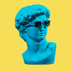 Statue. Earphone. Isolated. Gypsum statue of David's head. Man. Creative. Plaster statue of David's head in blue sunglasses. Minimal concept art.