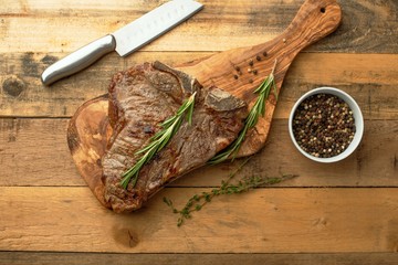 Marbled beef steak on a board with rosemary pepper, seasonings, with a knife on a wooden background, restaurant menu, gastronomy, tasty food. Horizontal photo, banner