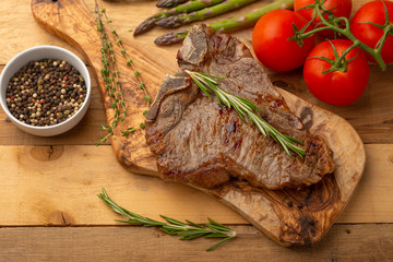Marbled beef steak on a board with rosemary pepper, spices, and fresh vegetables on a wooden background, restaurant menu, gastronomy, tasty food. Horizontal photo, banner