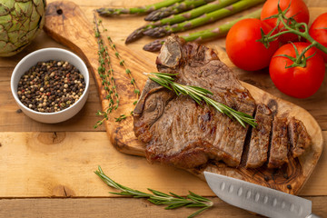Marbled beef steak on a board with rosemary pepper, seasoning, and fresh vegetables on a wooden background, restaurant menu, gastronomy, tasty food. Restaurant service