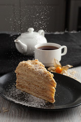 Slice of russian layered napoleon cake with vanilla cream filling and a cup of aroma black tea