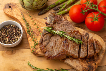 Marbled beef steak on a board with rosemary pepper, seasoning, and fresh vegetables on a wooden background, restaurant menu, gastronomy, tasty food. Restaurant service