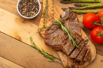 Marbled beef steak on a board with rosemary pepper, spices, and fresh vegetables, tomatoes and asparagus, artichoke, on a wooden background, restaurant menu, gastronomy, tasty food, restaurant service