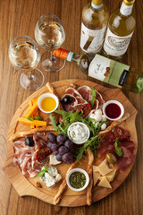 Fototapeta na wymiar Classic antipasto with assortment of cold snacks to wine: cheddar cheese, blue cheese, prosciutto, chorizo, olives, rucola, olive oil and pesto, served on a wooden dish
