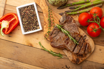 Marbled beef steak on a board with rosemary pepper, spices, and fresh vegetables, tomatoes and asparagus, artichoke, on a wooden background, restaurant menu, gastronomy, tasty food, restaurant service