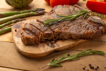 Marbled beef steak on a board with rosemary pepper, seasoning, and fresh vegetables on a wooden background, restaurant menu, gastronomy, tasty food. Restaurant service