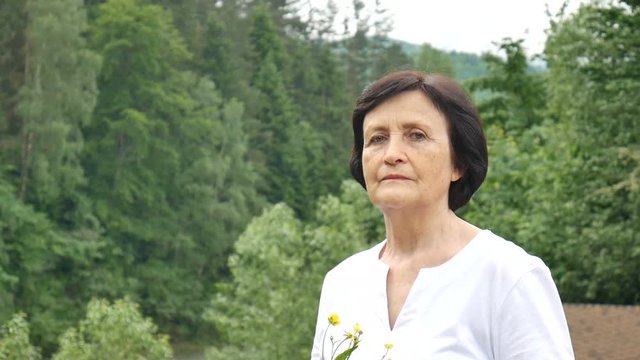 Close-up portrait of a beautiful elderly woman in the background of a mountain forest with wildflowers in her hand