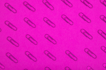 Violet paper clips pattern on pink background.