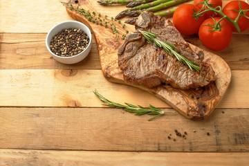 Marbled beef steak on a board with rosemary pepper, spices, and fresh vegetables on a wooden background, restaurant menu, gastronomy, tasty food. Horizontal photo, banner