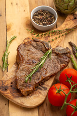 Marbled beef steak on a board with rosemary pepper, seasoning, and fresh vegetables on a wooden background, restaurant menu, gastronomy, tasty food. Restaurant service, verikalnoe photo, banner