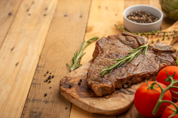 Marbled beef steak on a board with rosemary pepper, spices, and fresh vegetables on a wooden background, restaurant menu, gastronomy, tasty food. Horizontal photo, banner