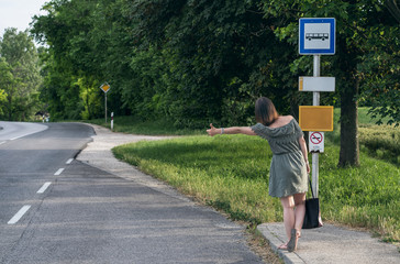 Young, caucasian woman hitchhiking in a bus stop near a European village in summertime.
