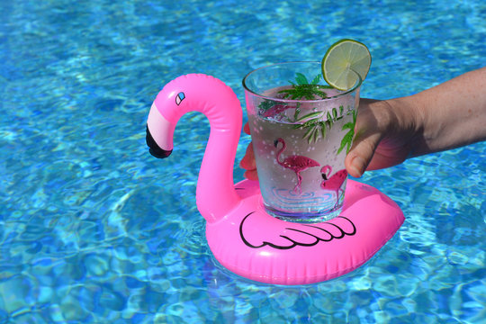 Woman Holding A Drink In A Pink Flamingo Inflatable Drinks Holder In A Swimming Pool.