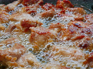 Close up of well-done deeping fried pork in boiling / bubbling cooking oil a frying pan - cook at home