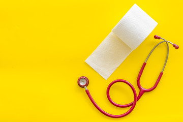 Toilet paper roll and stethoscope for proctology diseases concept on yellow background top view mock up