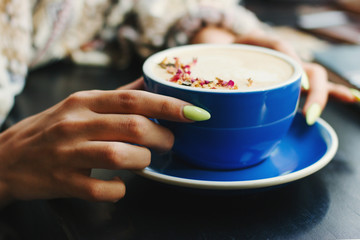 Coffee cup with latte art on wooden background in female hands. Beautiful foam, brown ceramic cup, space for text and design.