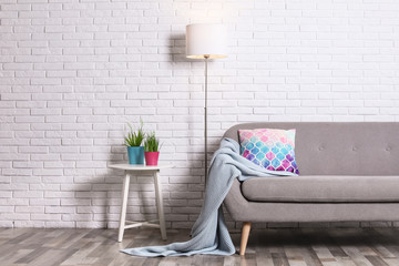 Cozy living room interior with sofa, pillow and plaid near brick wall. Space for text
