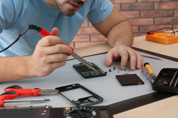 Technician repairing broken smartphone at table, closeup