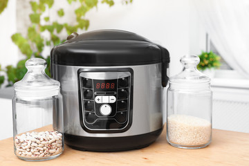 Jars with rice and beans near modern multi cooker on table in kitchen