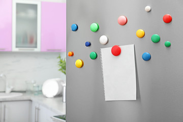 Empty sheet of paper with colorful magnets on refrigerator door in kitchen. Space for text