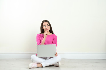 Young woman with laptop sitting on floor near light wall indoors. Space for text