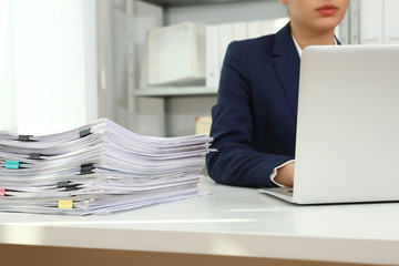 Female worker working with laptop near stack of documents in office, closeup