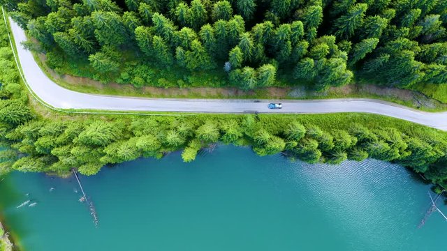 Aerial view of car driving through the fores and the lake on the side. Beautiful mountain road. Driving on the mountain road. Road trip. Mountain forest lake landscape. Car driving through pine forest
