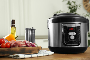 Modern multi cooker and products on wooden table in kitchen. Space for text