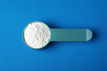 Scoop of protein powder on blue background, top view
