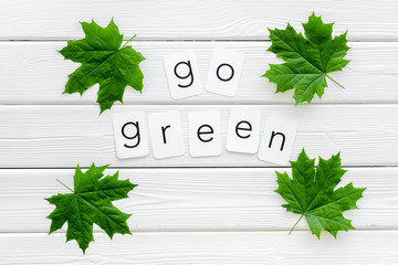 Go green text with green maple leaves on white wooden background top view