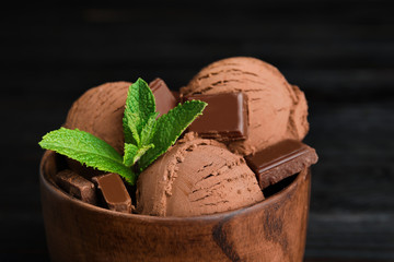 Wooden bowl of chocolate ice cream and mint on dark background, closeup