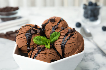 Bowl of chocolate ice cream with syrup and mint on table, closeup
