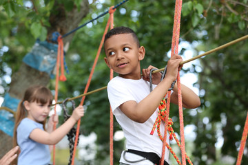 Little African-American boy climbing in adventure park. Summer camp