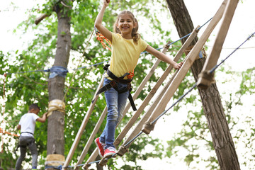 Naklejka na ściany i meble Little girl climbing in adventure park. Summer camp