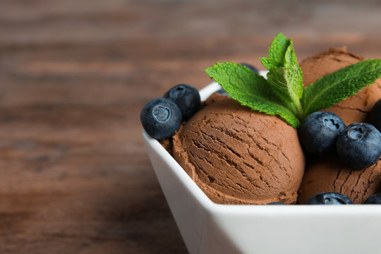 Bowl of chocolate ice cream and blueberries on wooden table, closeup. Space for text