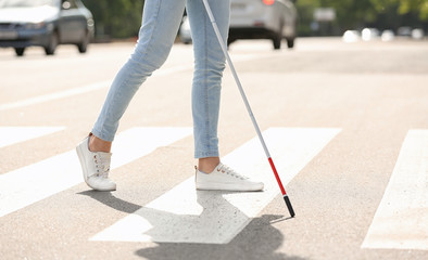 Blind person with long cane crossing road, closeup